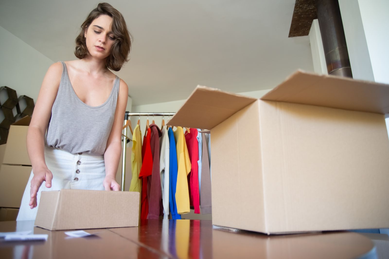 A founder packing orders in a small studio with a clothing rail behind her