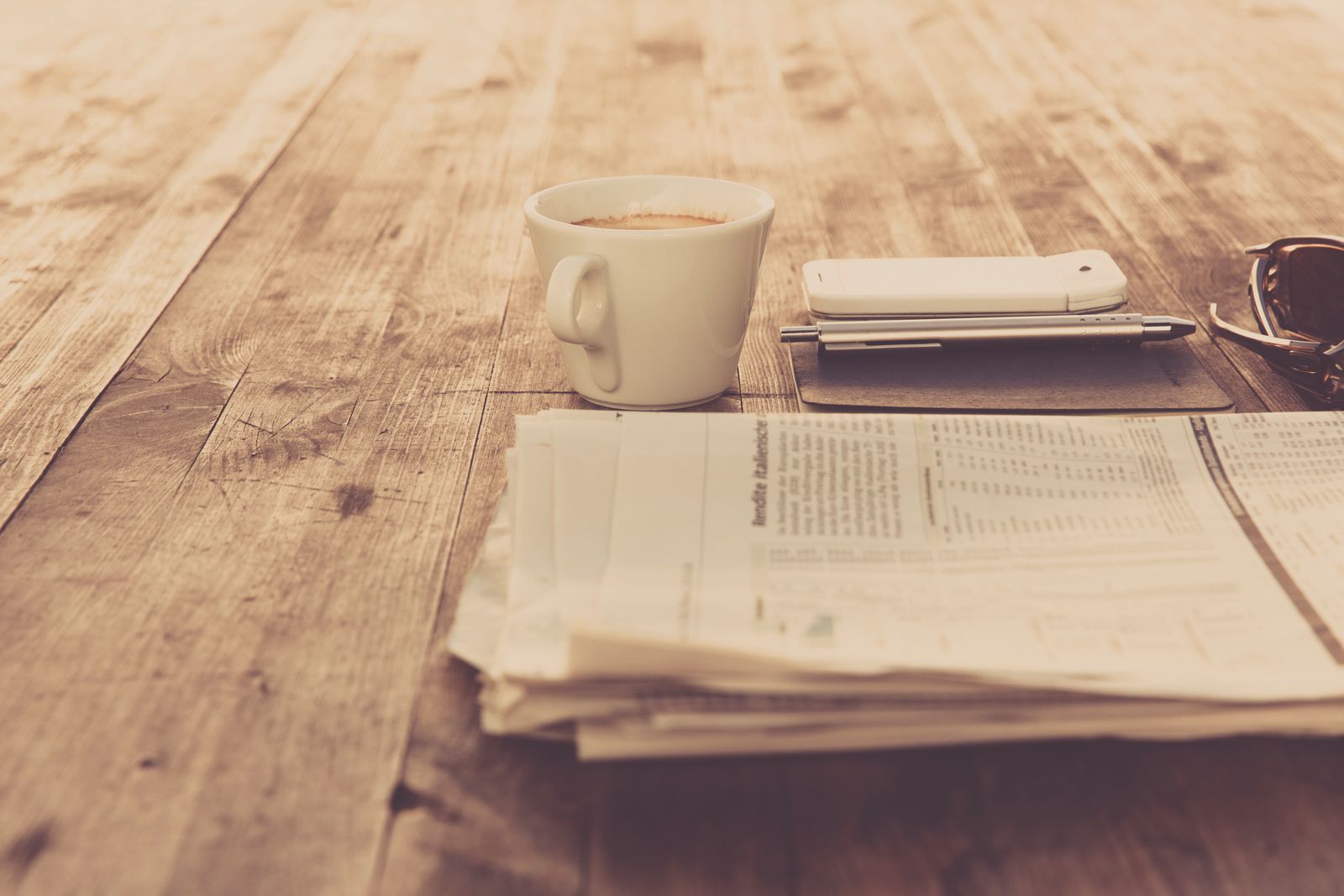 A folded newspaper and a cup of coffee on a wooden table